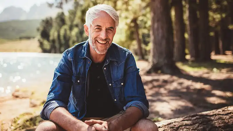A smiling older man sitting outdoors by a lake